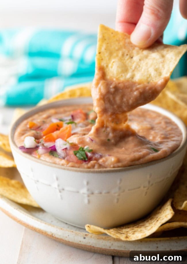 Hand dipping a tortilla chip into bean dip. 