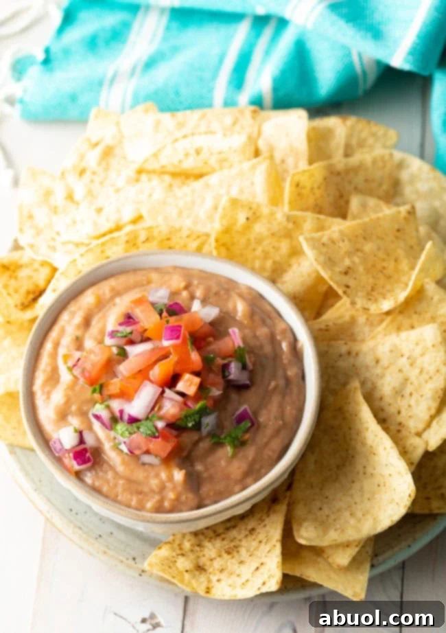 Pinto bean dip served in a bowl with pico de gallo on top next to a plate of tortilla chips. 