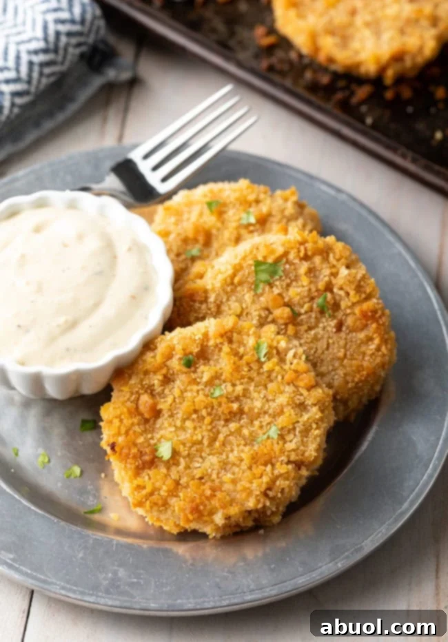 Three fried green tomatoes on a plate next to some sauce. 