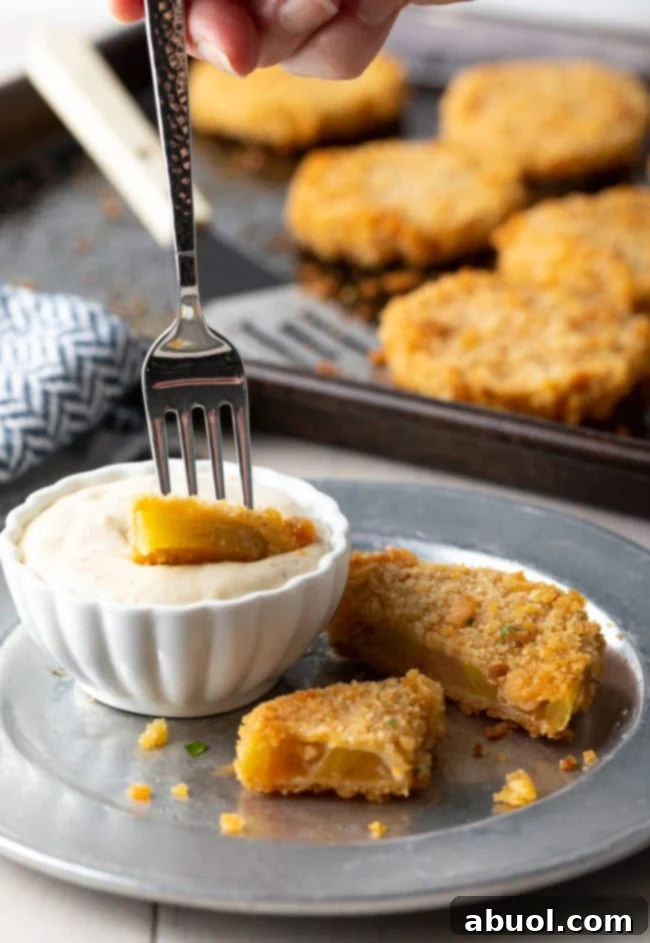 Fried green tomato on a plate cut into pieces with a fork dipping a piece into sauce. 