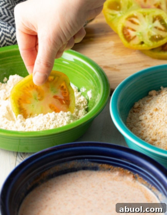 Hand dipping a slice of green tomato into flour. 