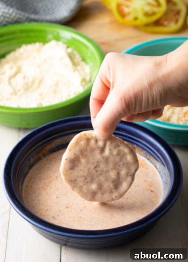 Hand dipping a green tomato slice into the buttermilk mixture. 