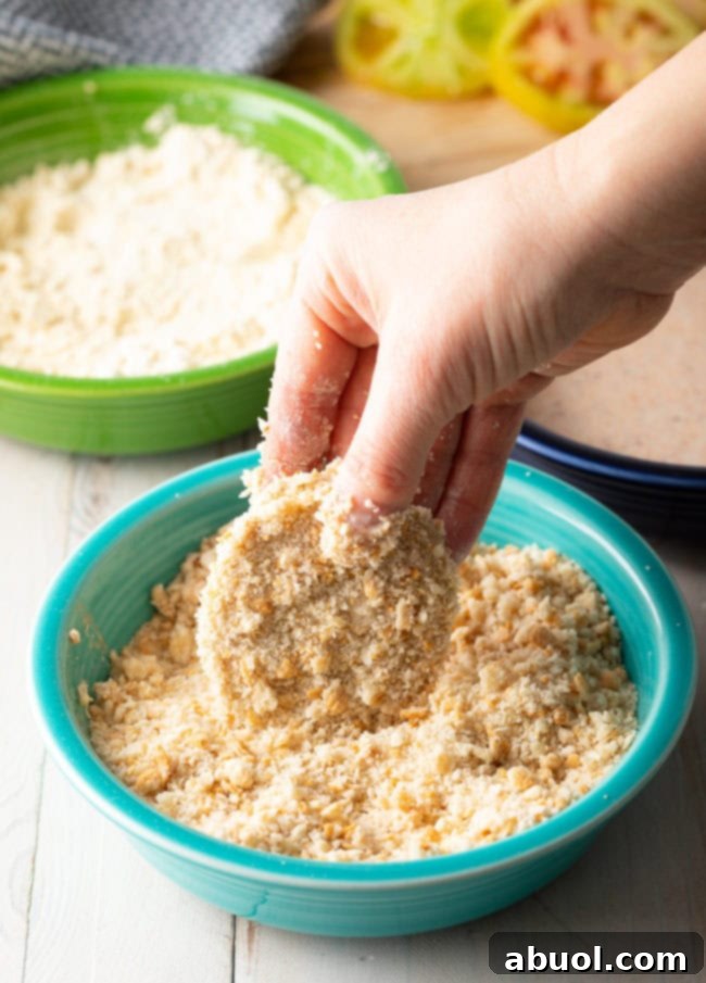 Hand dipping a green tomato in panko breadcrumbs. 