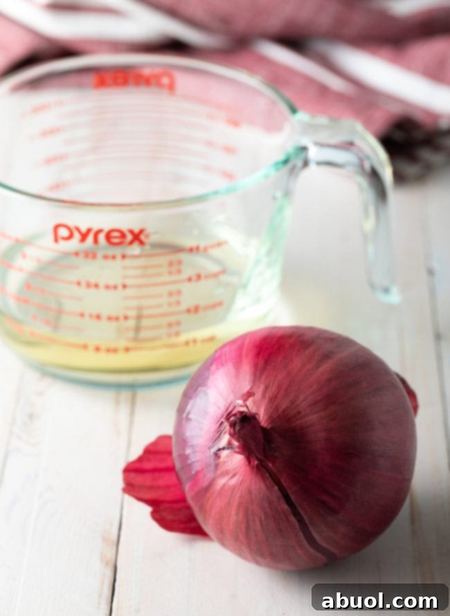 Red onion being sliced on a cutting board next to a small bowl of vinegar, ready for easy pickling