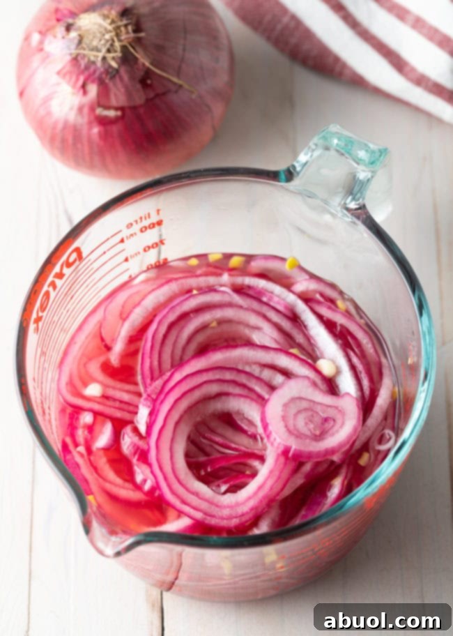 Quick pickled red onions in a measuring pitcher, showing the vibrant pink pickling liquid