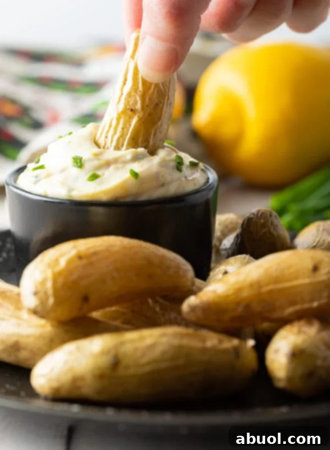 A hand dipping a fingerling potato into a bowl of aioli sauce on a plate with fingerlings.
