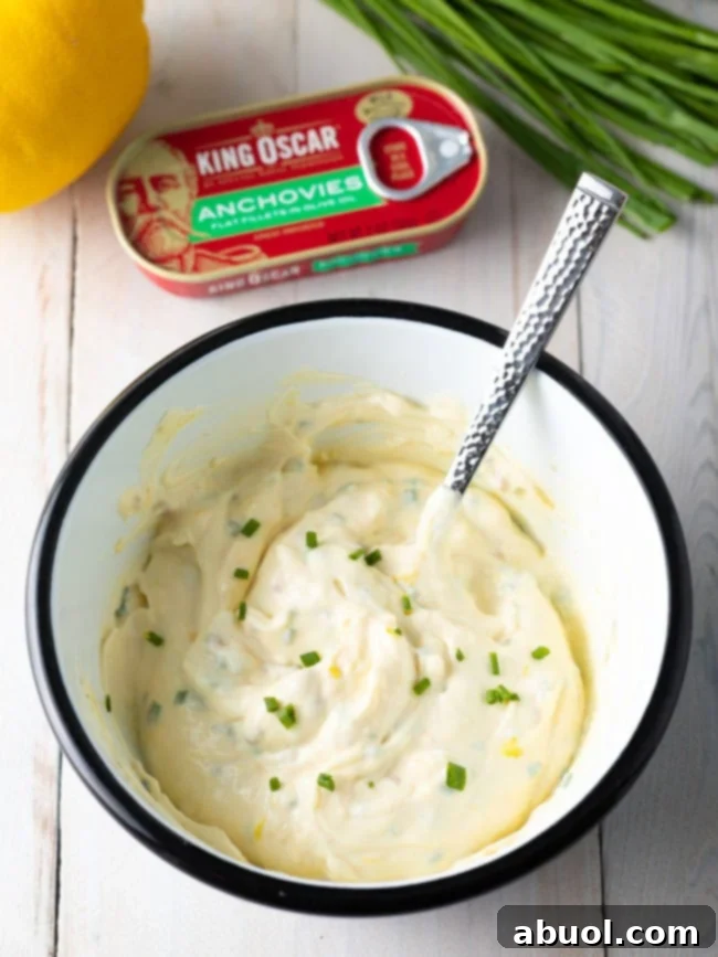 A white bowl with ingredients for aioli sauce with a spoon that has stirred the mixture.