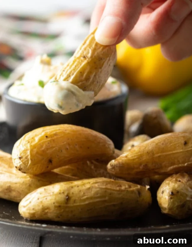 A hand dipping a fingerling potato into a bowl of aioli sauce on a plate with fingerlings.