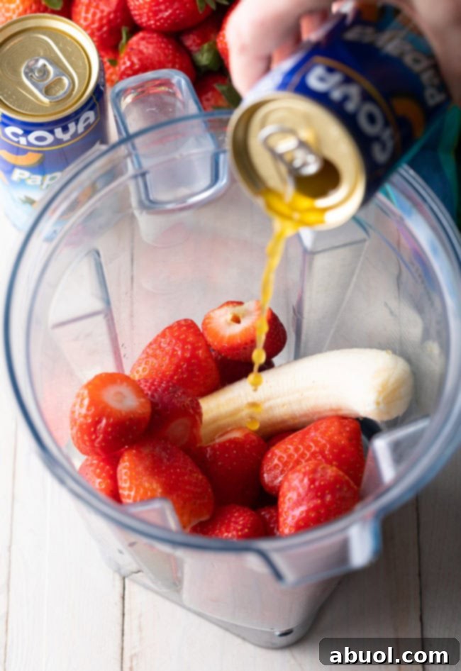 Banana and strawberries in a blender, with papaya nectar being poured over them.