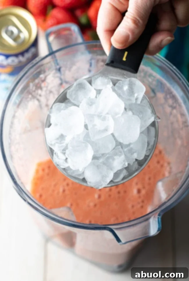 A cup of ice being added to the blender with the fruit puree.