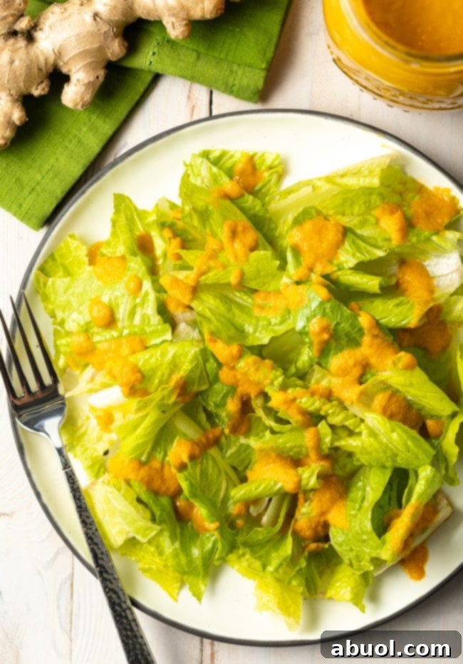 Simple green lettuce salad with a generous drizzle of vibrant carrot ginger dressing, served on a white plate, ready to eat and enjoy.