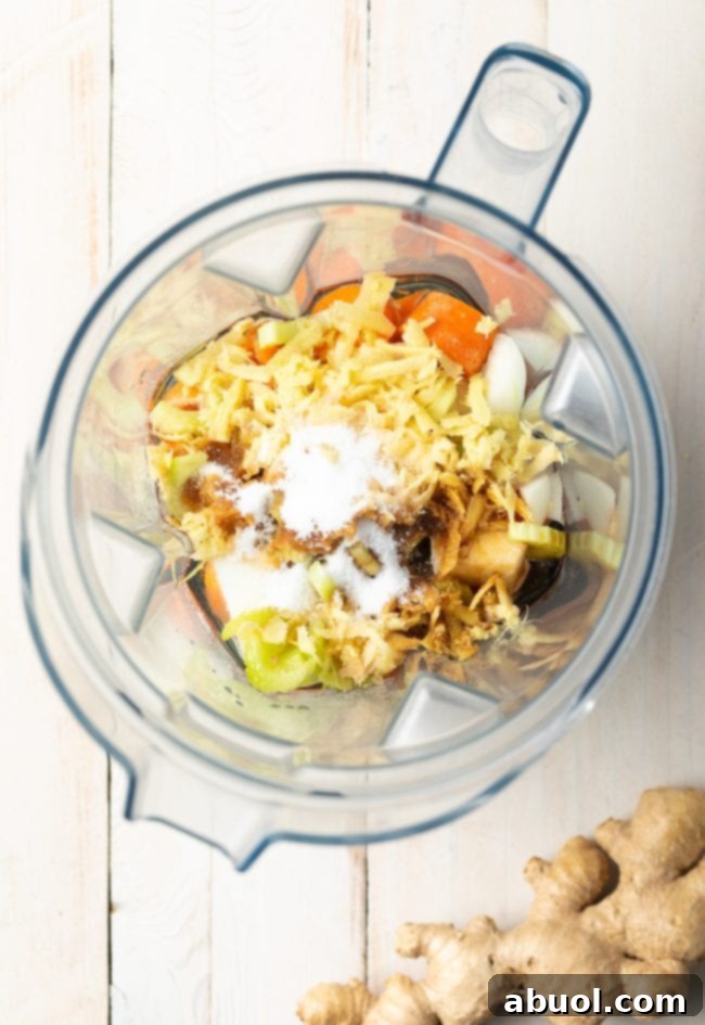 Raw ingredients for Japanese ginger dressing, including roughly chopped carrots, onion, celery, and a piece of fresh ginger, meticulously placed inside a blender jar, ready for blending.