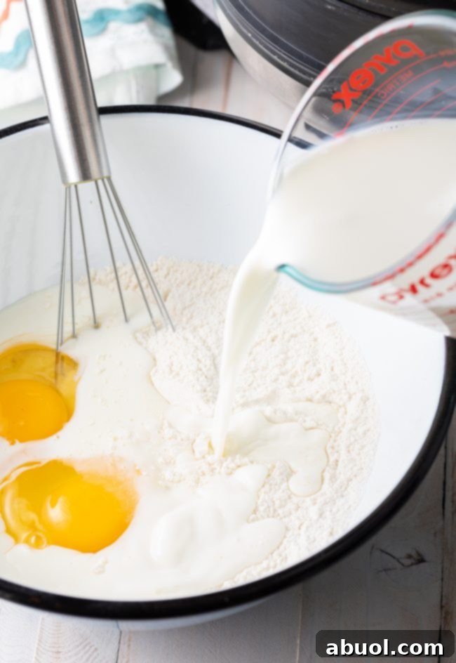 Waffle batter being gently mixed in a bowl as milk is poured in, illustrating the liquid ingredient incorporation.