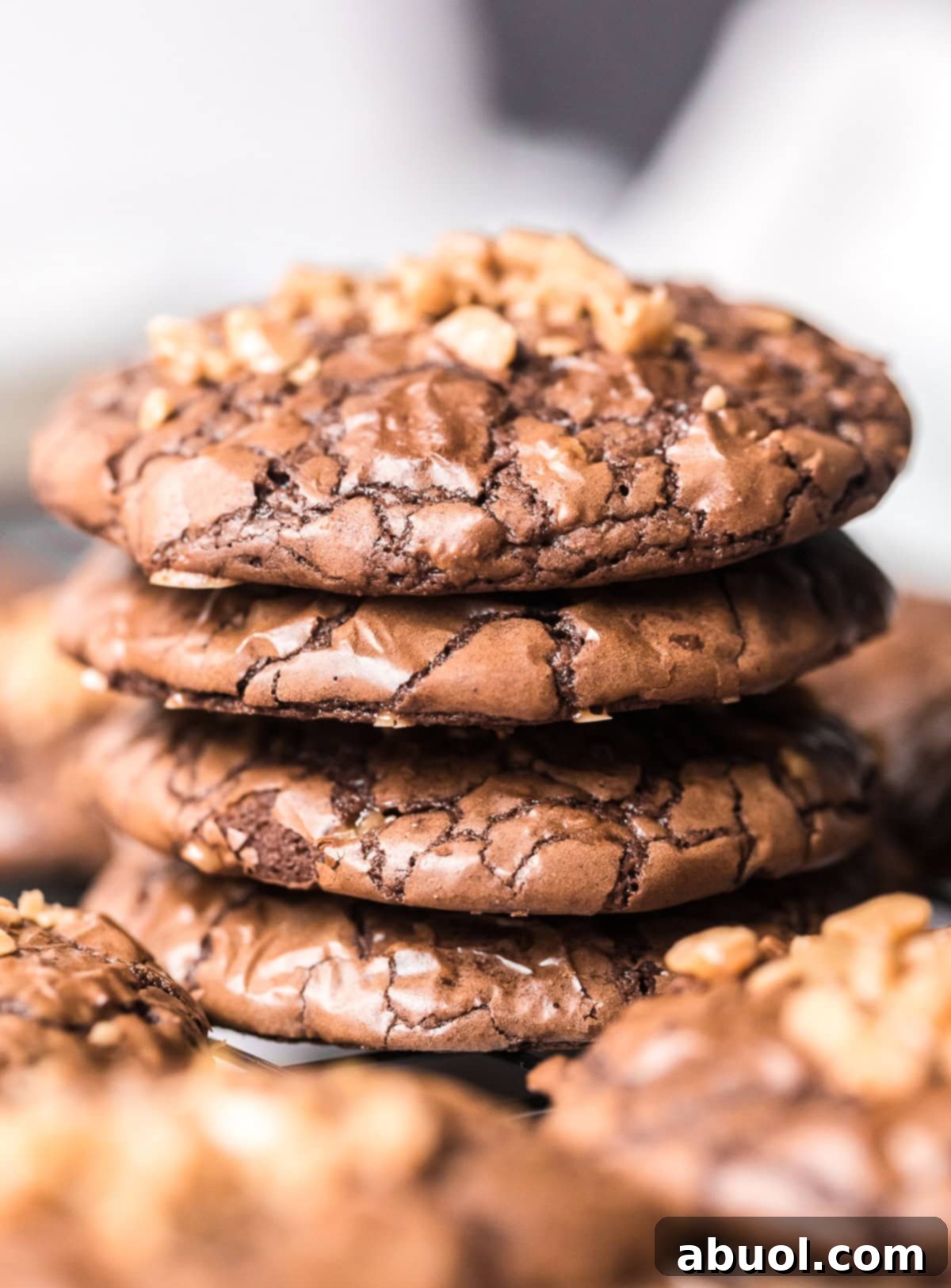 A stack of freshly baked Toffee Brownie Cookies, showing their perfectly fudgy interior and crisp, crinkly tops, adorned with visible toffee bits.