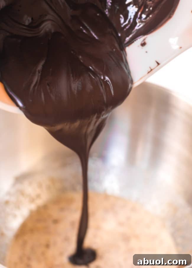 Pouring rich, melted chocolate into the brownie cookie dough, showing the glossy texture.