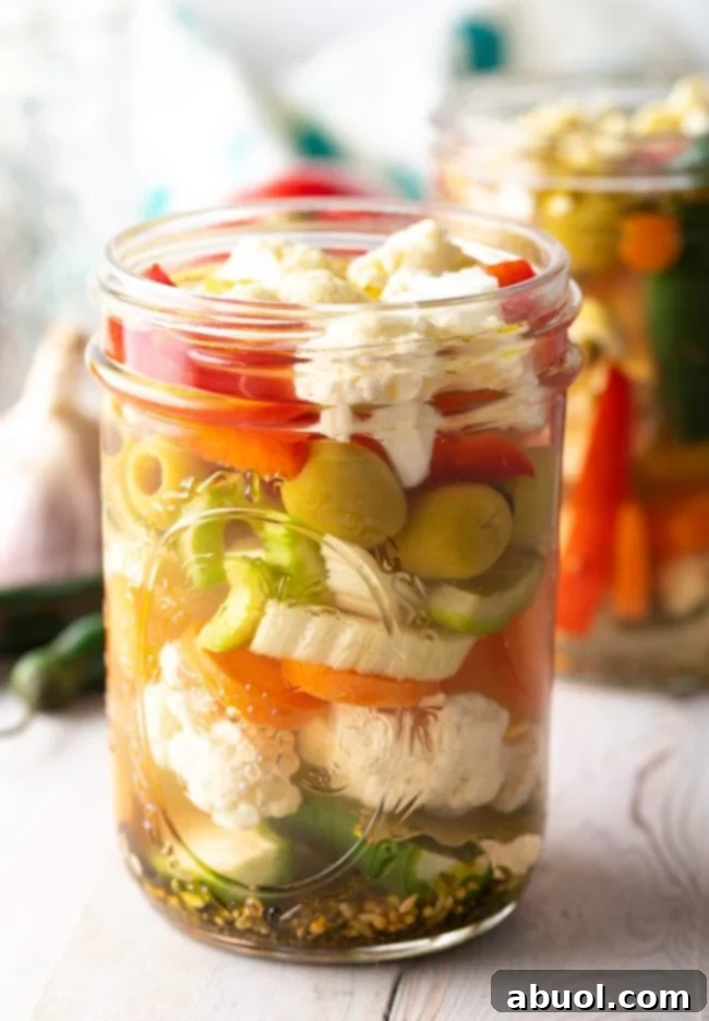 Zesty Italian Giardiniera 4 Two jars of Giardiniera Pickled Veggies, with fresh vegetables blurred in the background.
