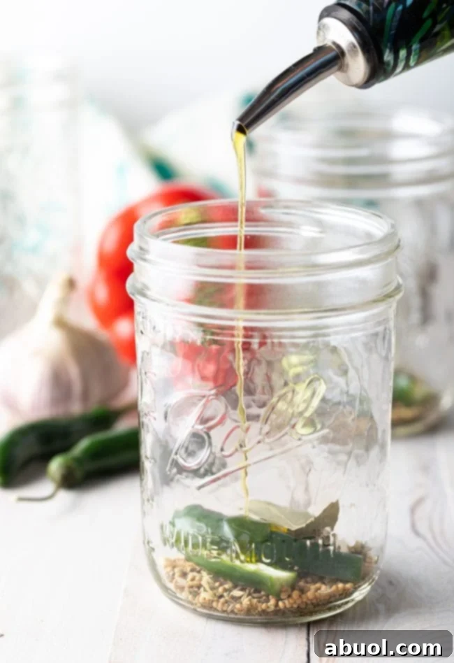Zesty Italian Giardiniera 7 Spices and serrano chili in a jar with olive oil being poured over them.