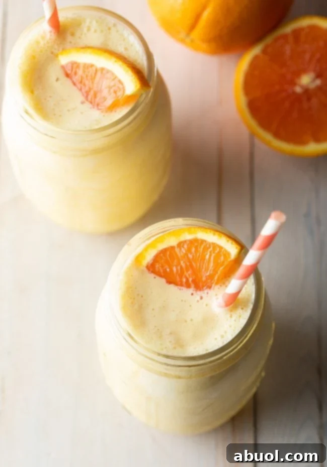 Overhead shot of two Orange Julius smoothies in jars, garnished with fresh orange slices and straws.
