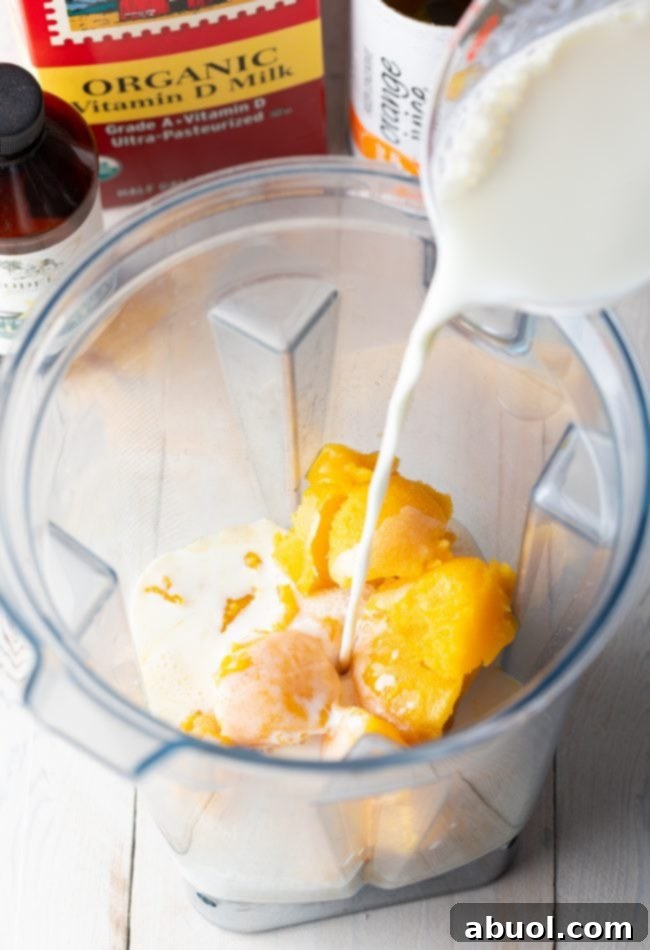 Pouring milk into a blender with frozen orange juice concentrate already inside.