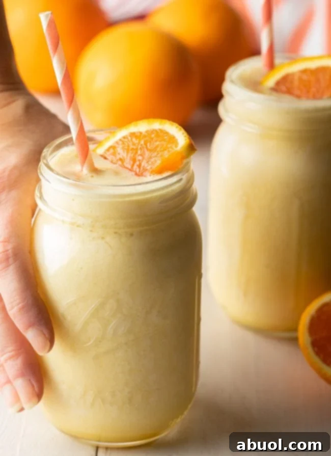 A hand reaching for a jar filled with frothy Orange Julius smoothie, showing its tempting texture.