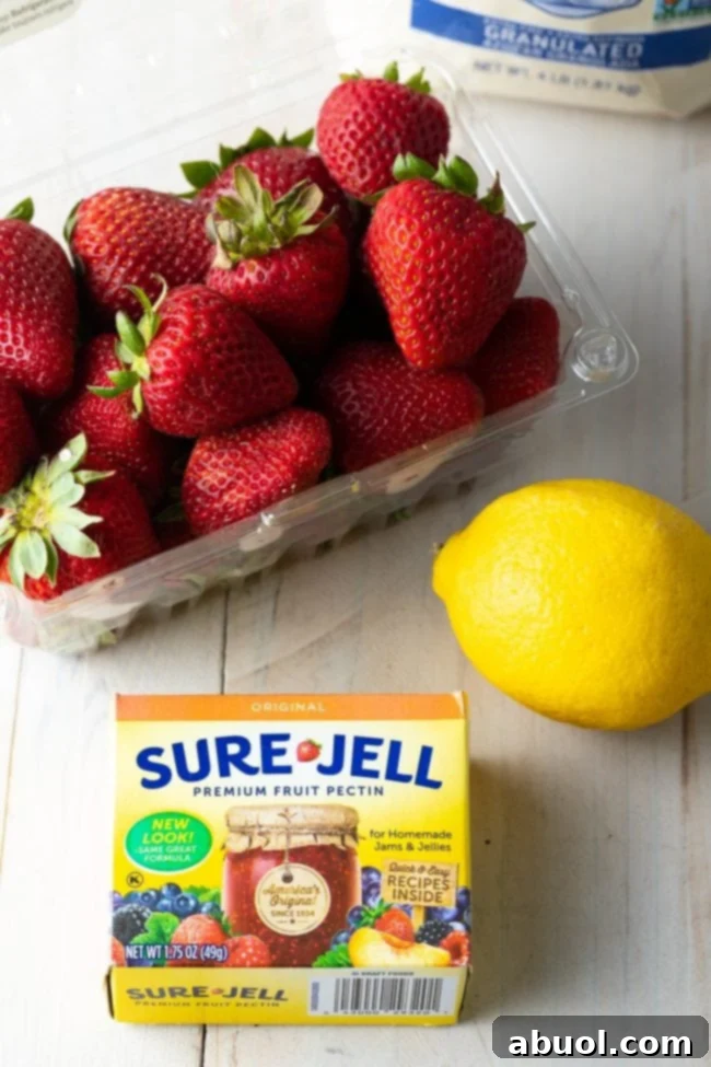 Fresh strawberries, a bright lemon, and a packet of powdered pectin laid out on a clean counter, representing the essential ingredients for making delicious homemade freezer jam.