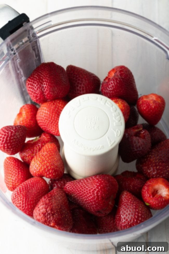 A top-down view of vibrant whole strawberries being processed in a food processor, ready to be transformed into delicious jam.