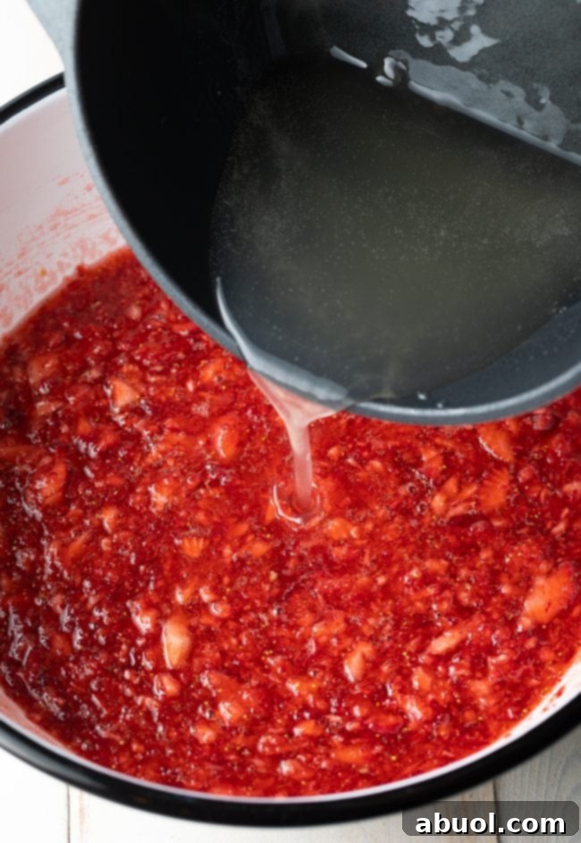 A steady stream of hot pectin syrup being poured into a bowl of mashed strawberry puree, demonstrating a key step in making freezer jam.