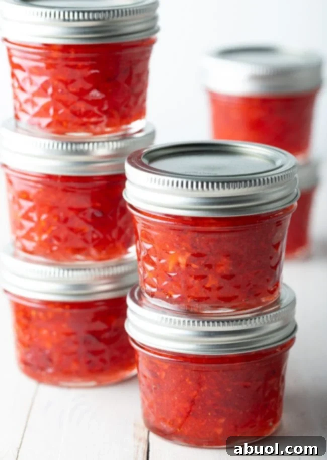 Neatly stacked glass canning jars filled with various homemade freezer jams, showcasing a colorful and organized collection of preserves.