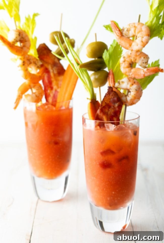 Closeup view of 2 Bloody Mary cocktails garnished with shrimp, bacon, celery, olives and carrots. 