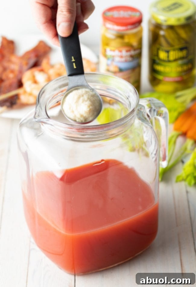 Hand adding horseradish into pitcher. 