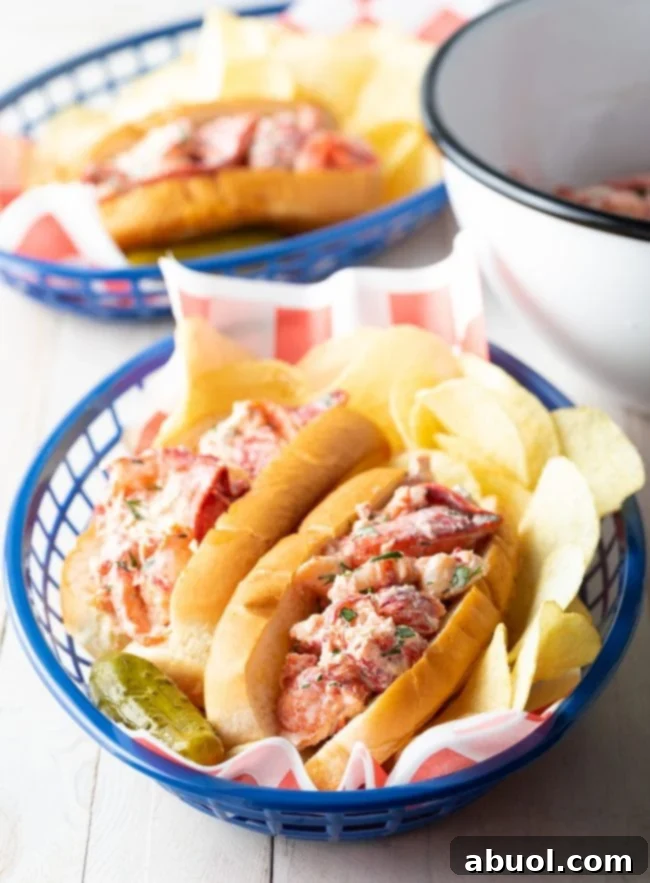 Beautifully plated lobster rolls in individual serving baskets, complete with potato chips and a side of pickles, ready for a feast.