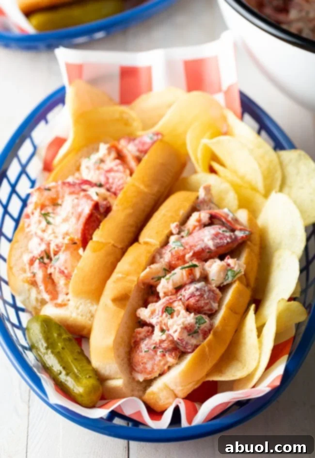 A single, perfectly assembled lobster roll nestled in a basket, accompanied by crispy chips and a dill pickle spear, ready to be enjoyed.