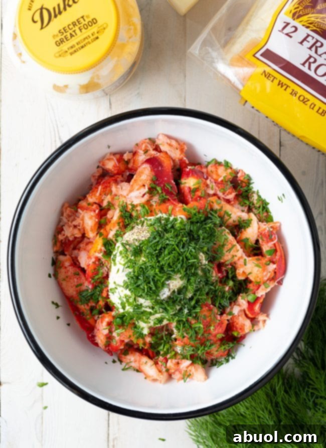 Cooked lobster meat in a mixing bowl, with freshly chopped herbs and a dollop of mayonnaise ready to be folded in.