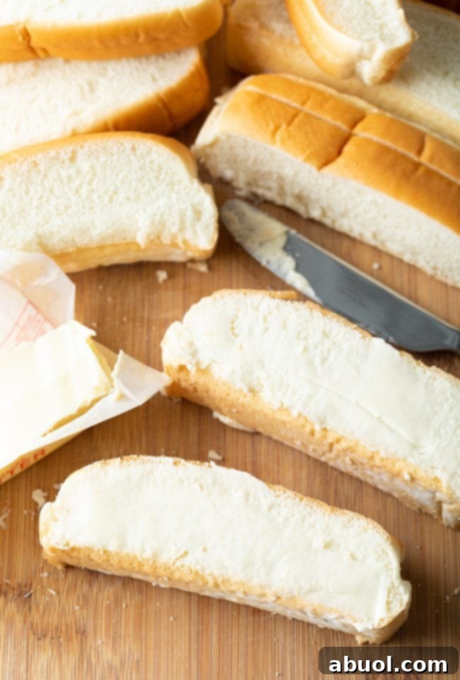 Softened butter being meticulously spread onto the flat sides of a New England bun.