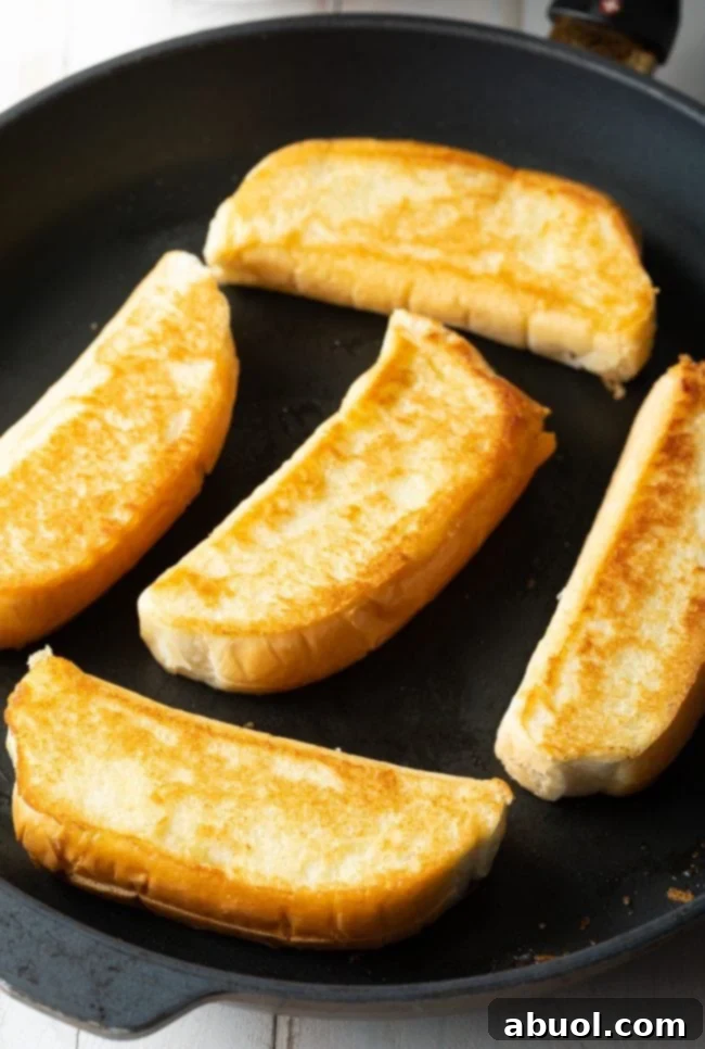 Several New England buns being toasted on a hot griddle, achieving a perfect golden-brown crispness.