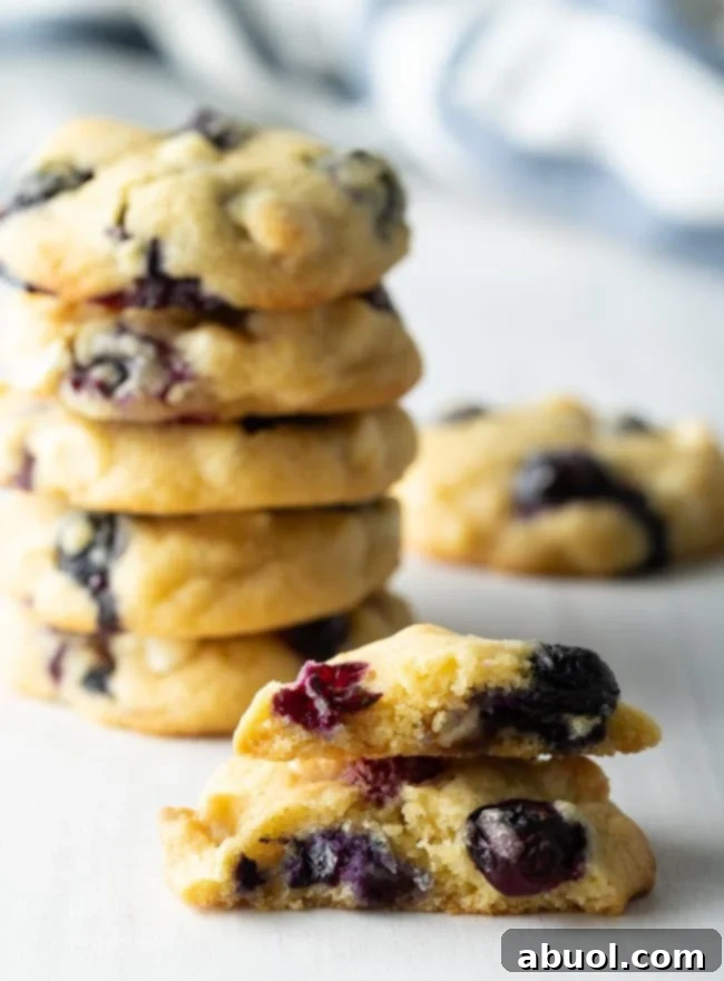 Blueberry white chocolate chip cookies stacked on top of each other with one broken in half to see the inside.