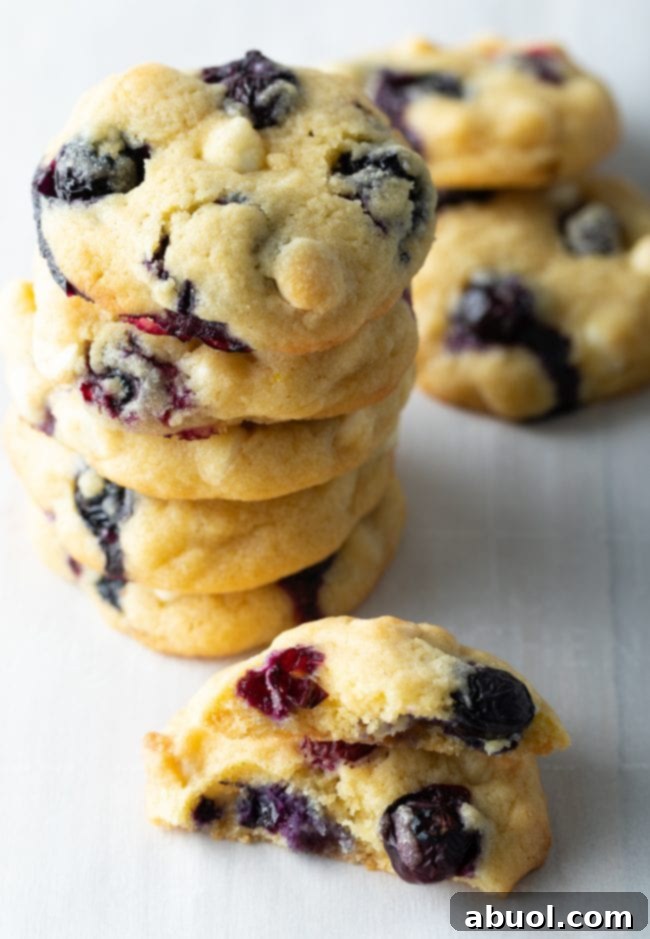 Stack of blueberry cookies next to a cookie broken in half to see the inside.