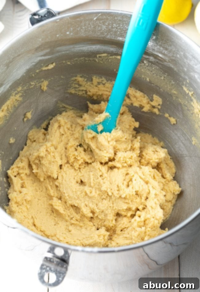 Cookie dough in a large metal mixing bowl with a blue spatula.