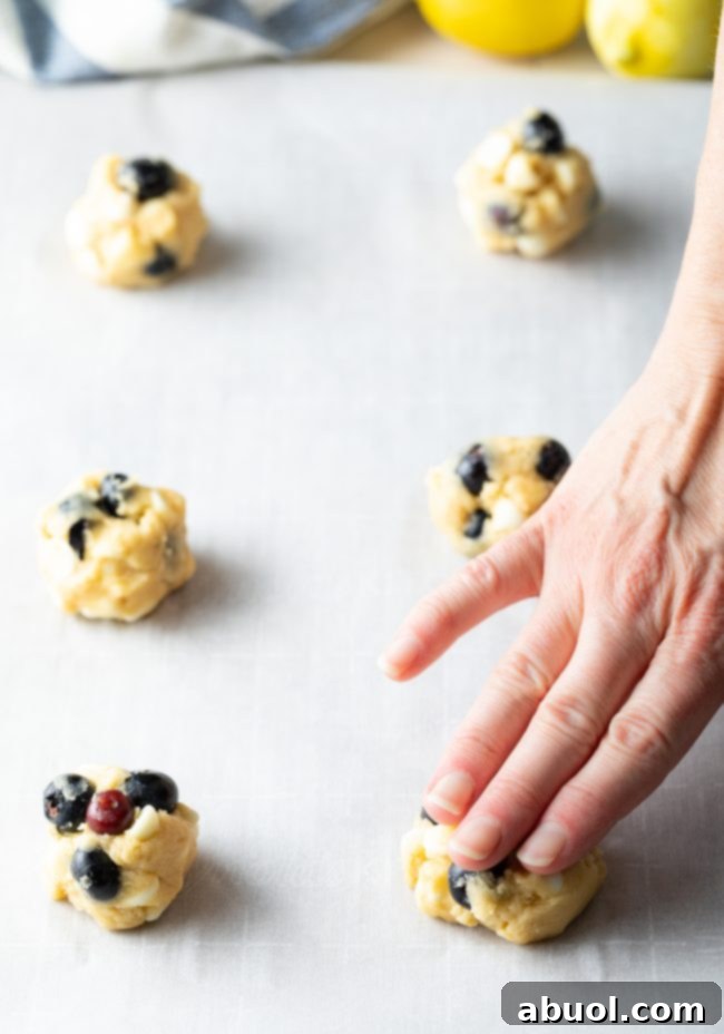 Cookie dough balls on a baking sheet lined with parchment paper with a hand pressing the ball dough a bit.