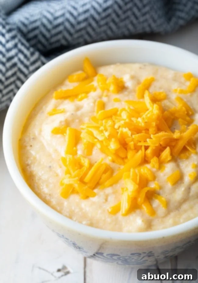 Creamy Cheese grits recipe in a white bowl with shredded cheddar cheese on top. 