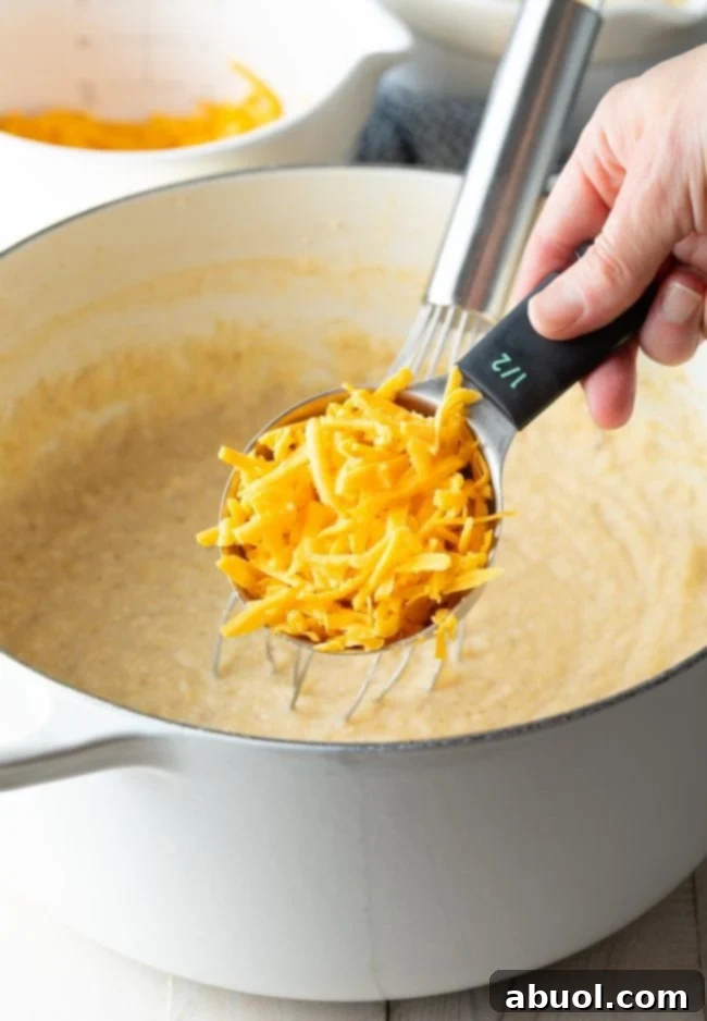 Grits in a stockpot with cheddar cheese being stirred in. 