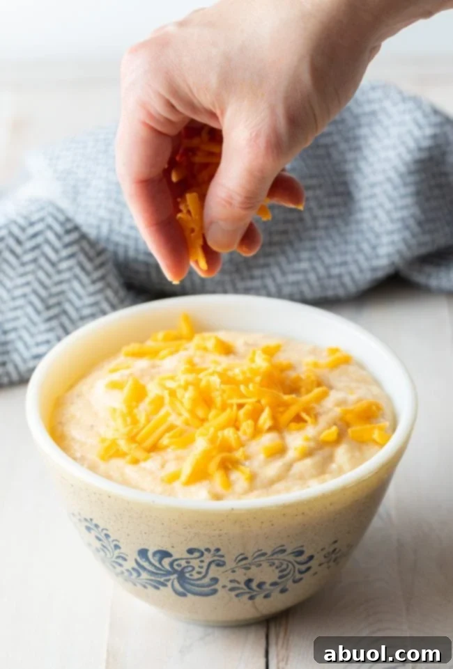 Bowl of grits with a hand above it sprinkling cheese on top. 