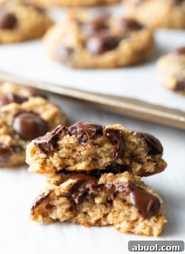 Two banana bread cookies, made with oatmeal and chocolate chips, are artfully halved and stacked, showcasing their soft, chewy interior.