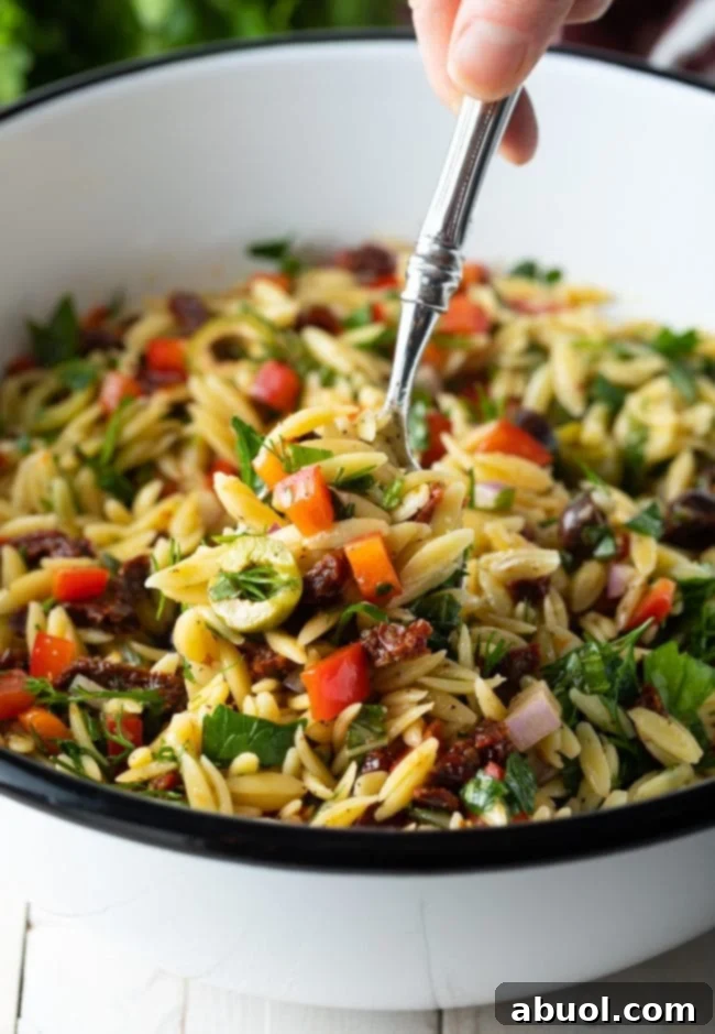 Orzo salad with lemon vinaigrette in a bowl with a spoon scooping some up, showcasing its vibrant colors and textures.