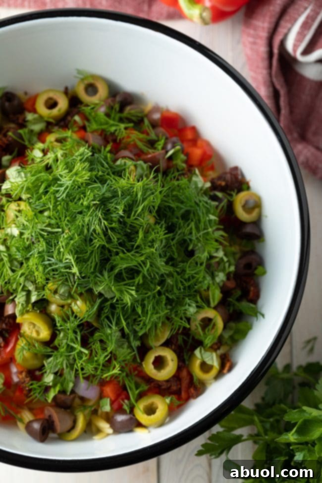 A bowl of freshly chopped herbs, including basil, dill, and parsley, ready to be added to the orzo salad.