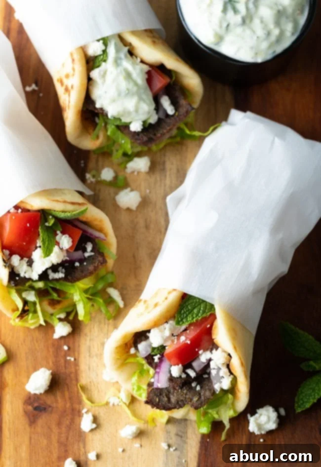 Overhead shot of three assembled lamb gyros wrapped in parchment paper.