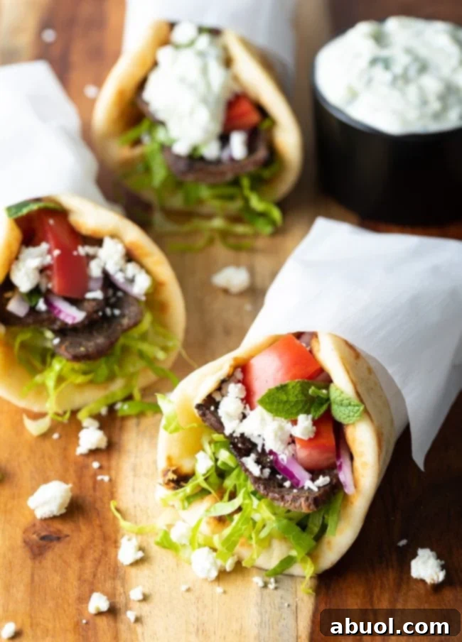 Lamb gyros assembled and wrapped in paper on a wooden surface.