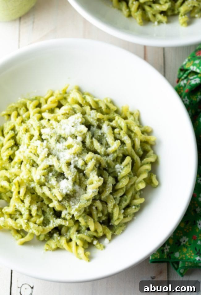 Fusilli pasta coated in pesto and served in a white bowl with parmesan on top. 