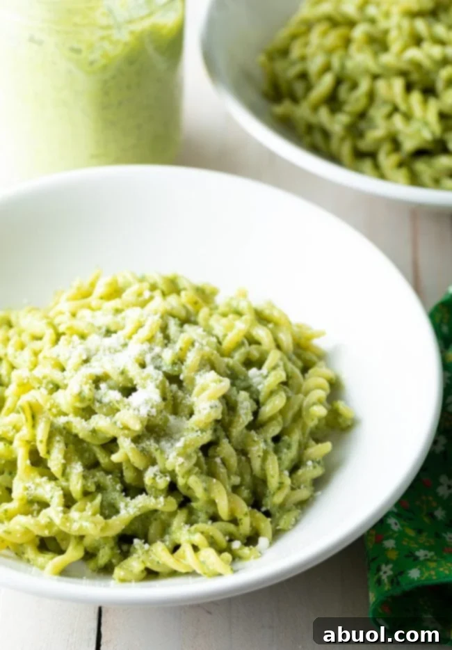 Pesto pasta in white bowls with a jar of pesto next to them.