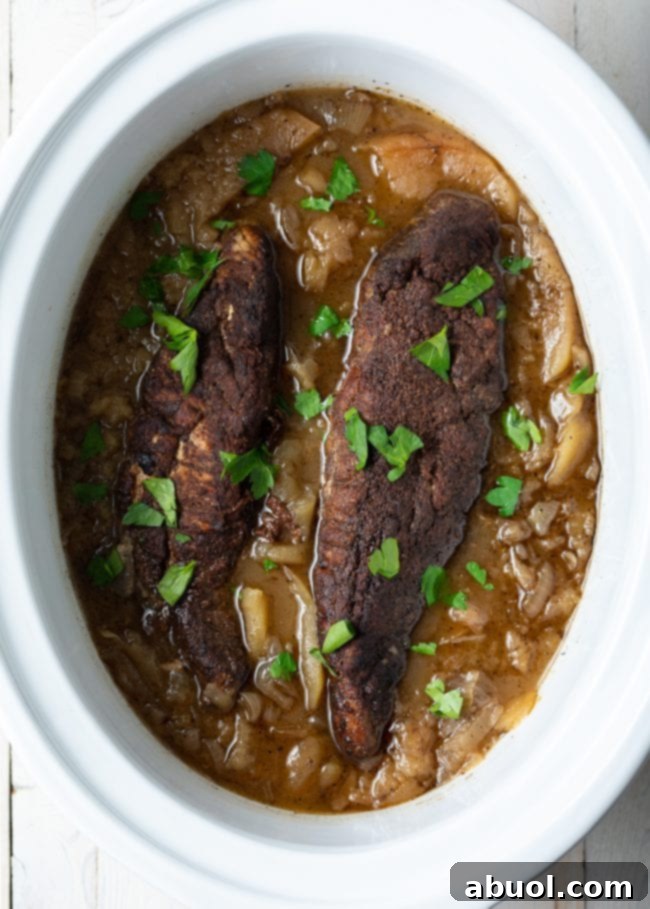 Pork tenderloins nestled amidst a sweet and savory apple and onion sauce, simmering gently in the crockpot.